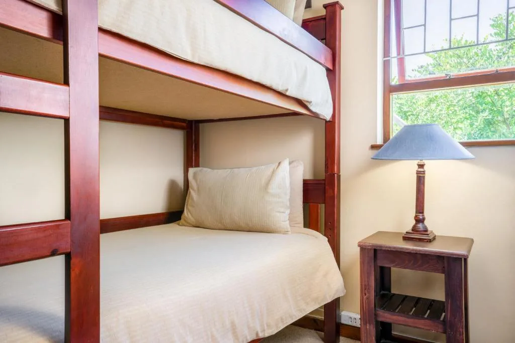 Bunk bed with white linens and wooden frame, bedside lamp and window