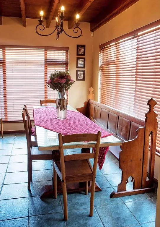 Warm dining room with wooden table, chairs, fresh flowers, and bright windows