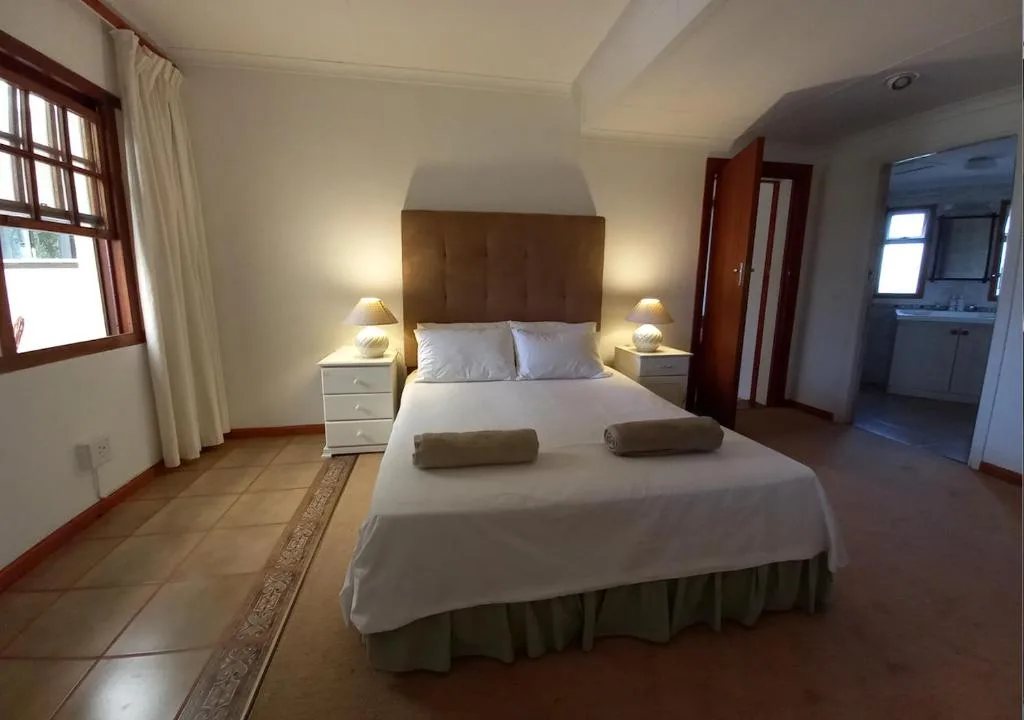 Spacious bedroom with queen bed, bedside tables, warm lighting, and ensuite bathroom access
