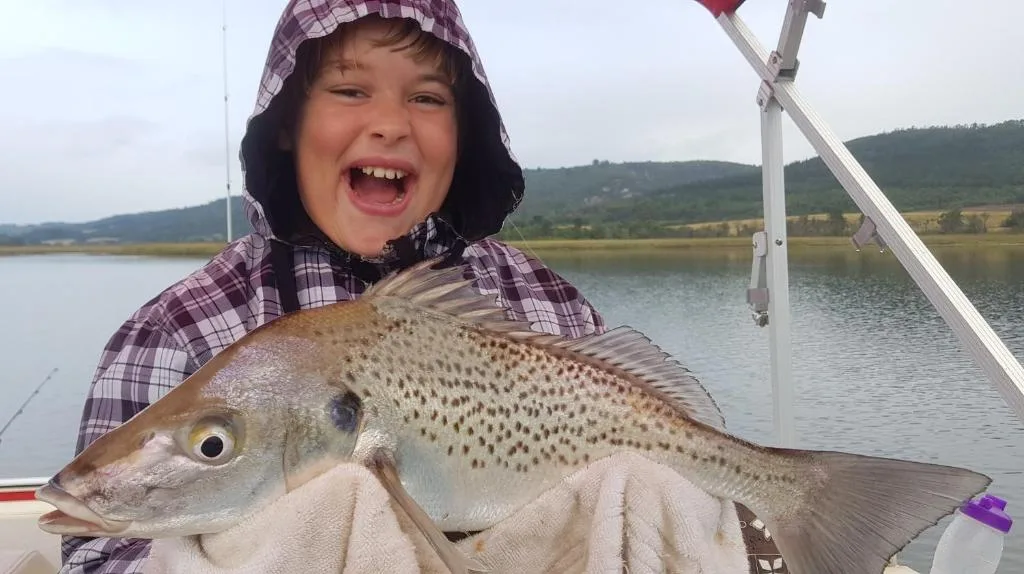 Child holding large freshly caught trout on fishing boat