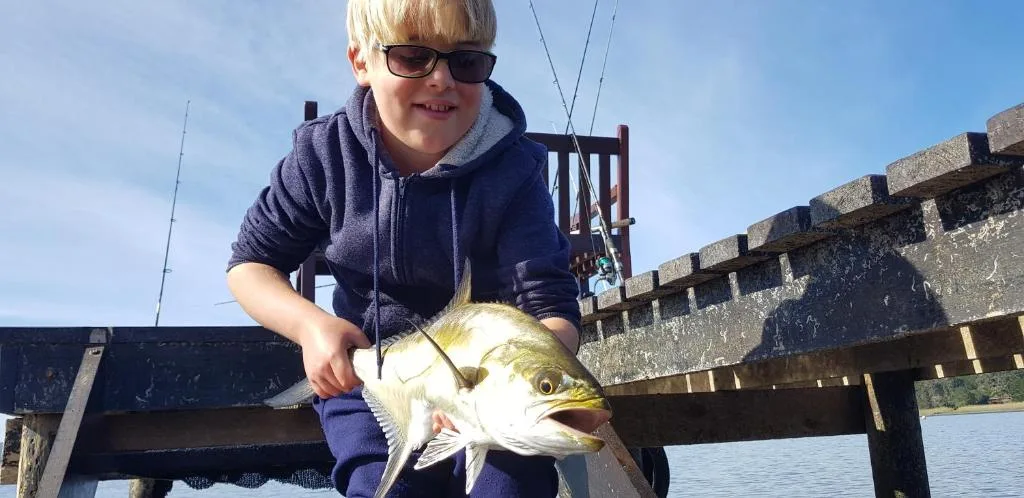 Child holding caught fish on wooden lakeside pier