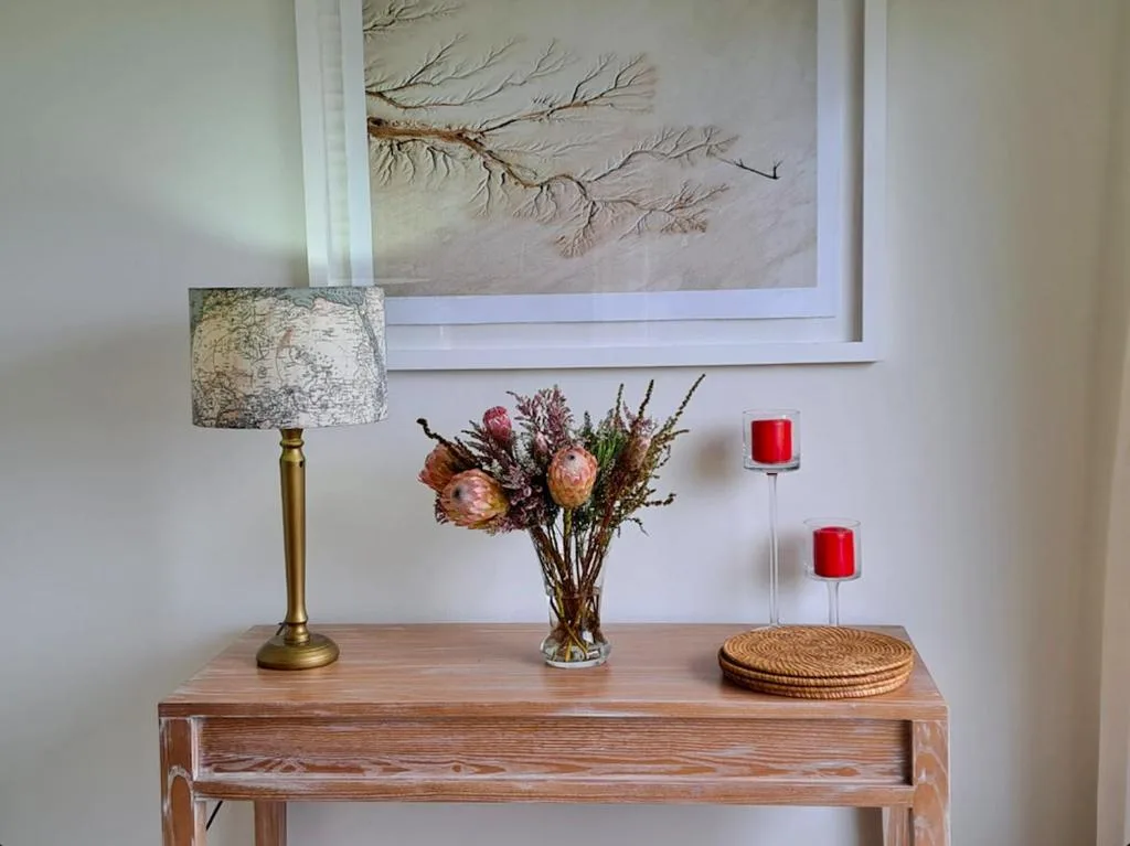 Wooden console table with decorative lamp, dried flowers, and framed wall art