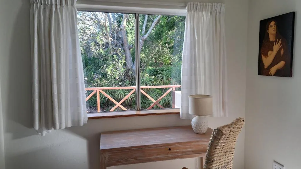 Wooden desk with lamp and woven chair facing garden view window