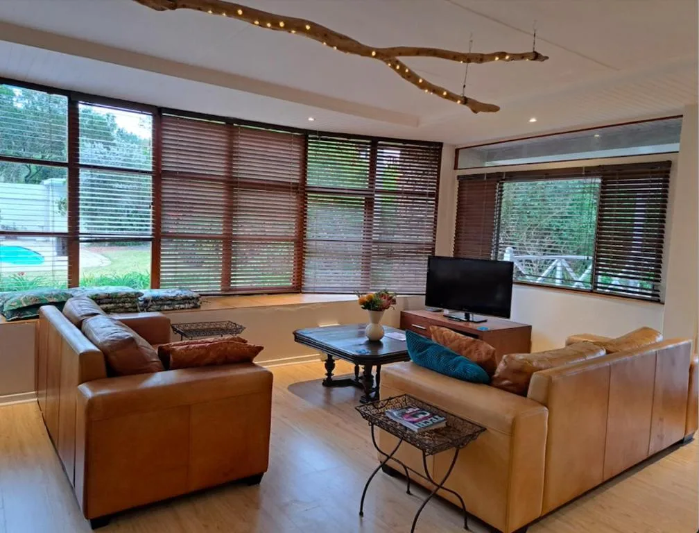 Spacious lounge with leather seating, TV, and large windows overlooking garden