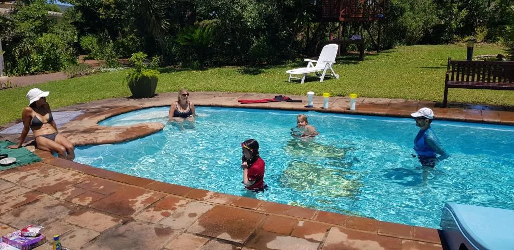 Family swimming and relaxing in bright blue pool surrounded by lush green lawn
