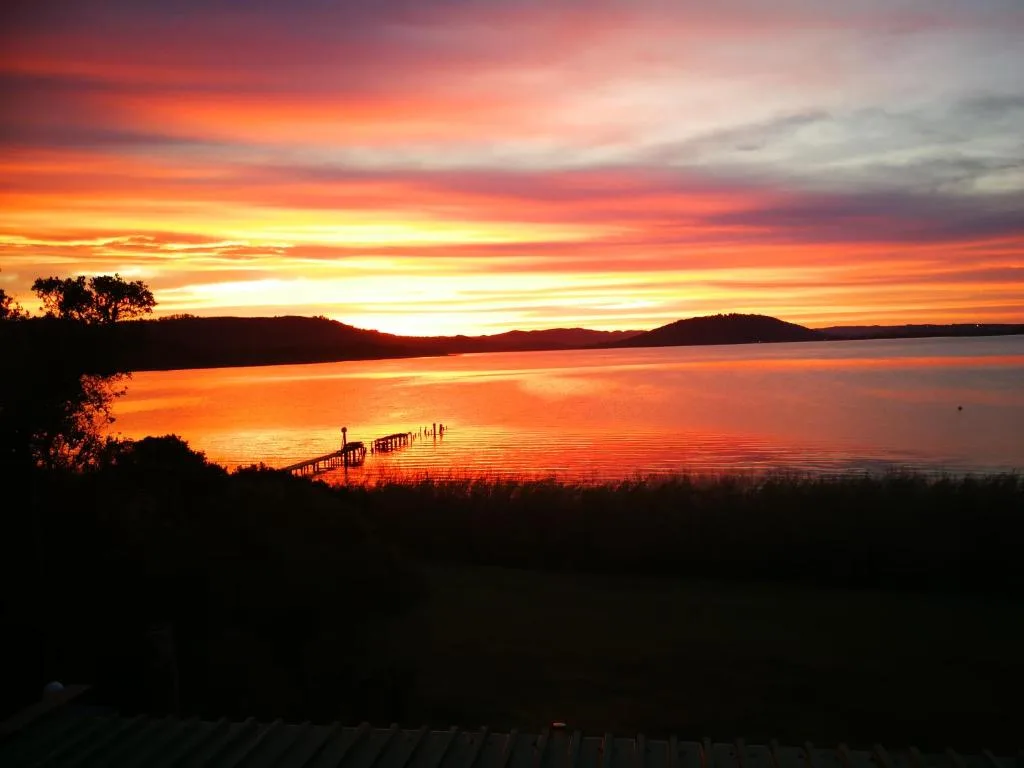 Vibrant sunset over Swartvlei Lake with wooden jetty and mountains
