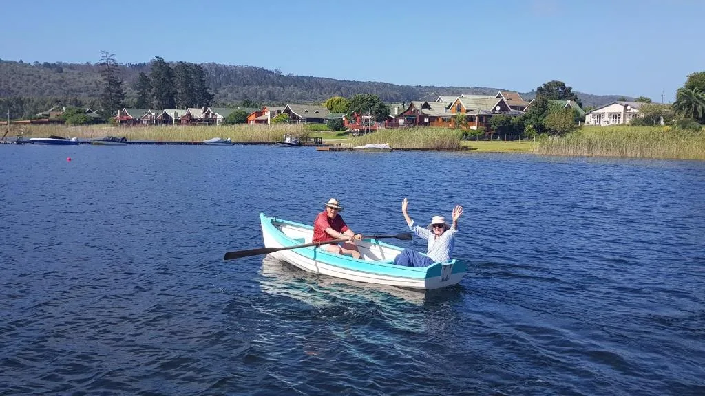 Scenic lake view with rowboat, waterfront homes, and forested hills beyond