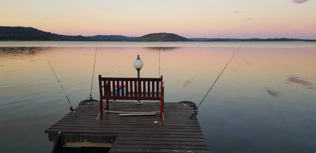 Serene sunrise over Swartvlei Lake with wooden dock and fishing rods