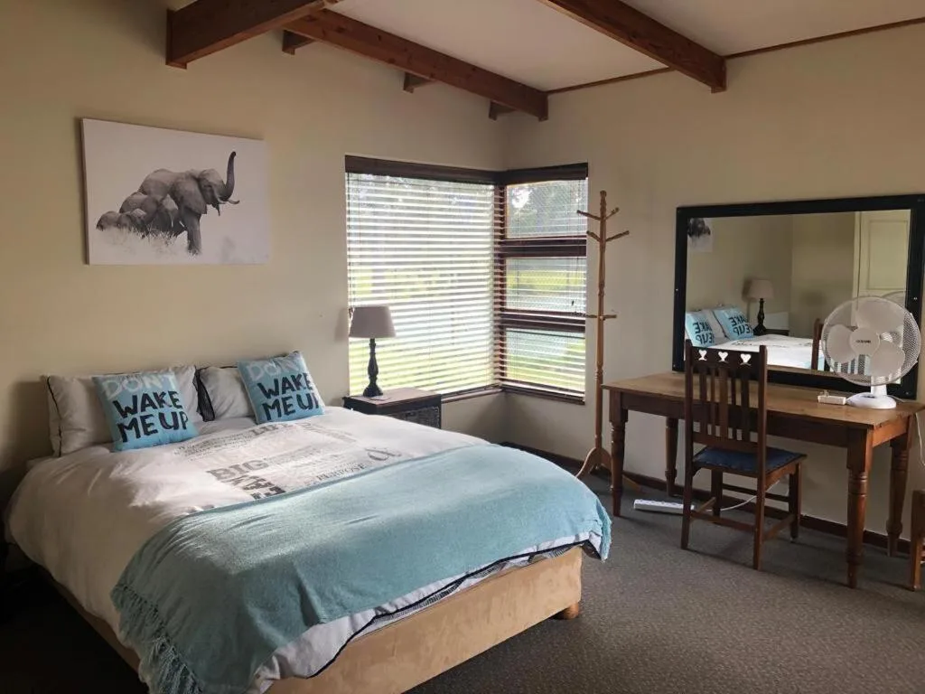 Bright bedroom with queen bed, desk, mirrored vanity, and large windows overlooking garden