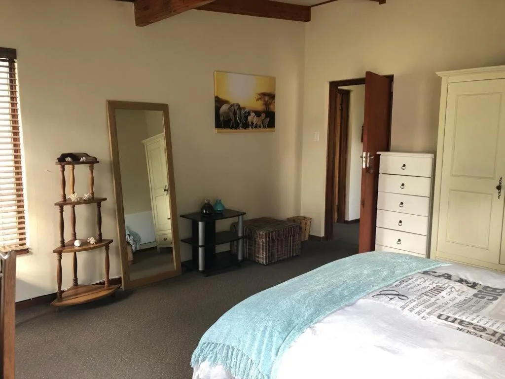 Spacious bedroom with bed, wooden furniture, mirror, and natural light