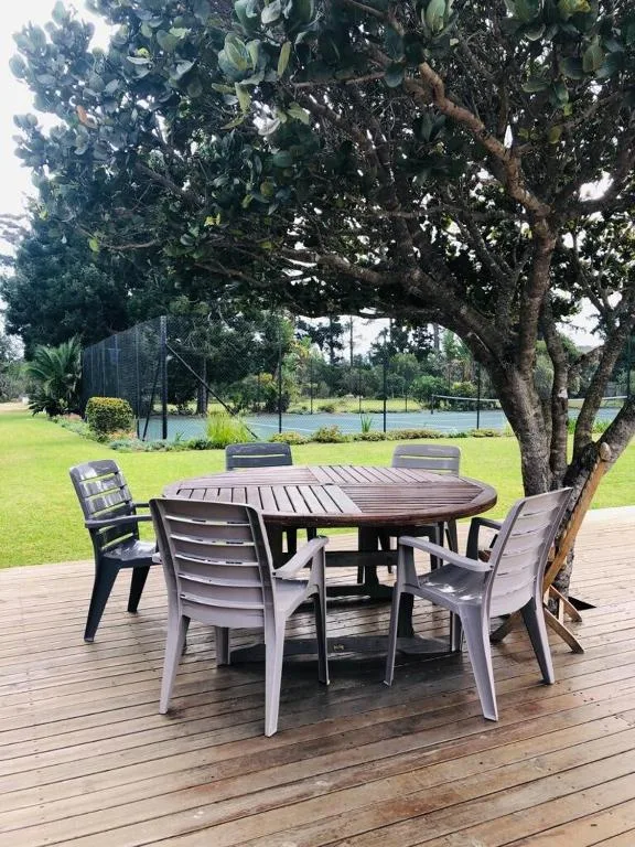 Wooden deck with round dining table and chairs under mature tree, overlooking lake
