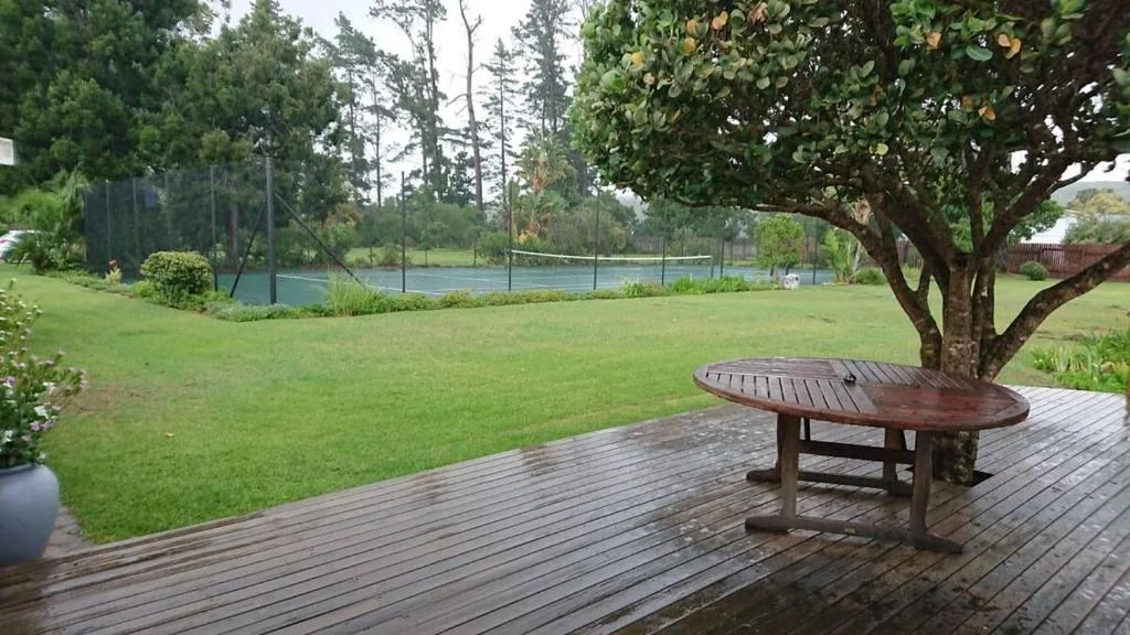Wooden deck with oval table overlooking lush garden and tennis court