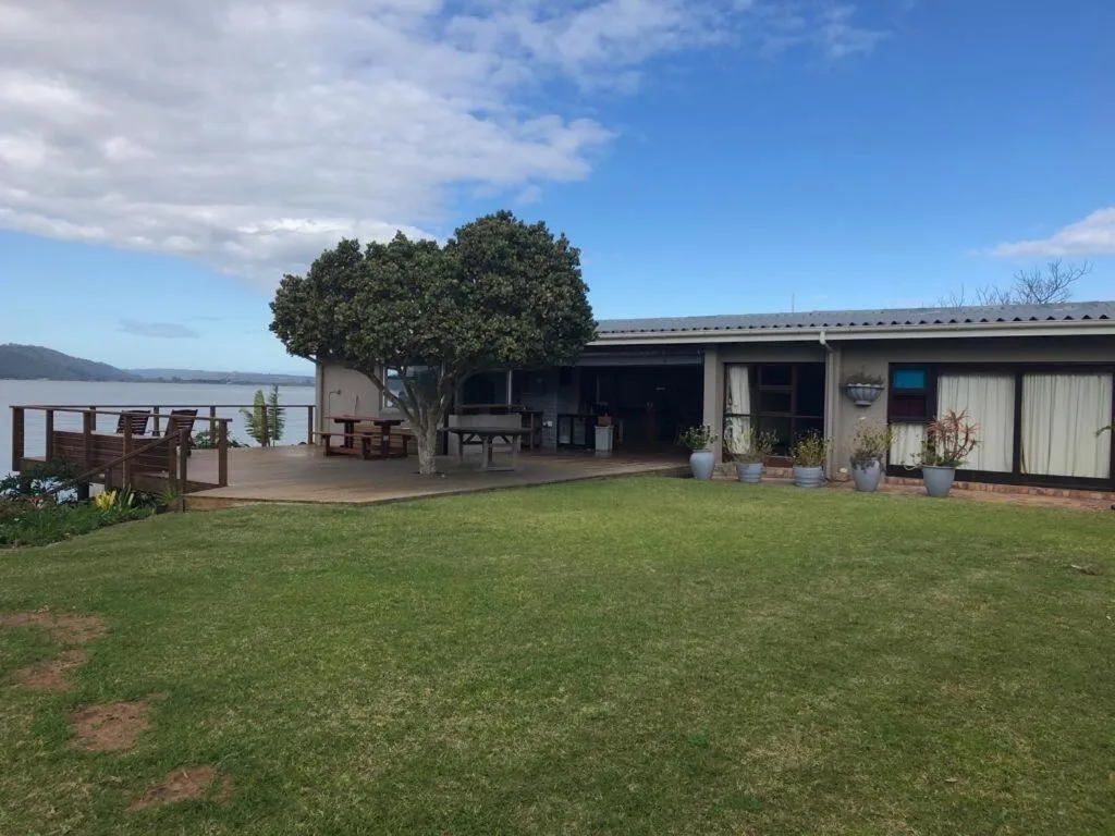 Single-story waterfront home with deck overlooking lake and manicured lawn