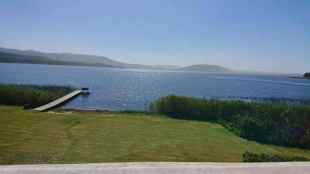 Scenic lake view with mountains, green lawn, and wooden jetty pier