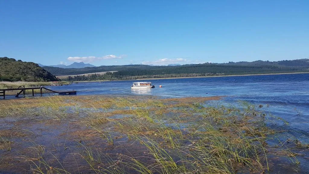 Scenic lagoon vista with mountains, forests, and moored boat beyond