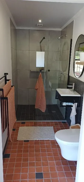 Modern bathroom with walk-in shower, terracotta tiles, and round mirror