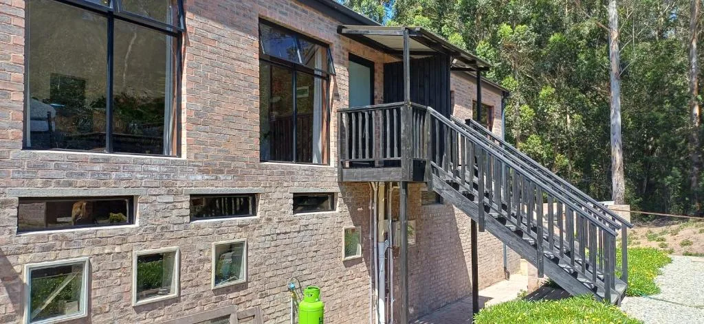 Modern brick building with deck railing and forest surroundings, Garden Route