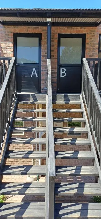 Twin entrances with black doors labeled A and B, wooden stairs, brick facade