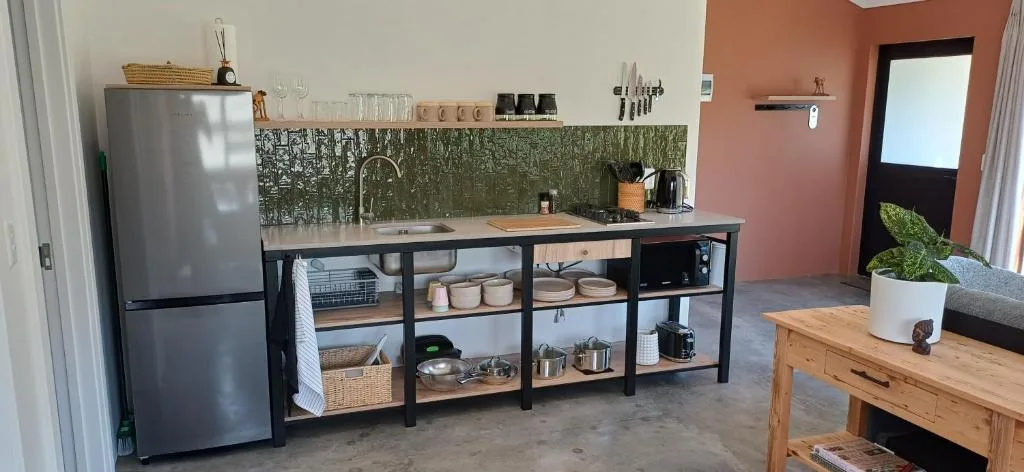 Modern kitchenette with stainless steel fridge, green tile backsplash, and black metal shelving
