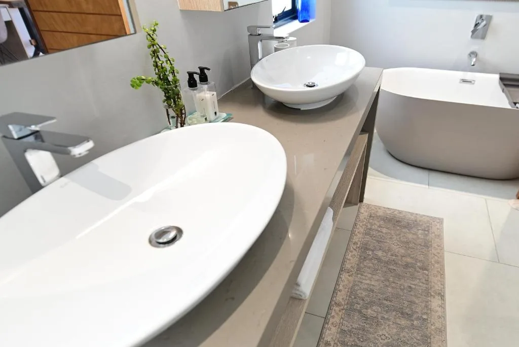 Modern bathroom with dual vanities, round white basins, and decorative plants