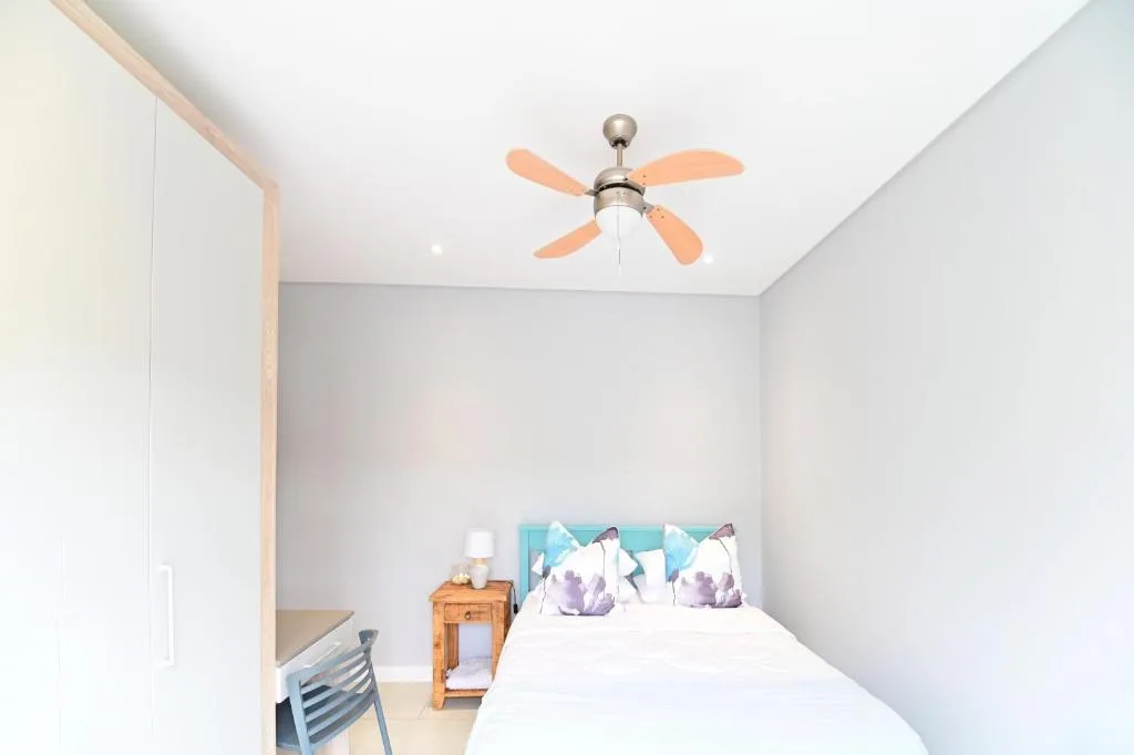 Bright bedroom with queen bed, purple accent pillows, ceiling fan
