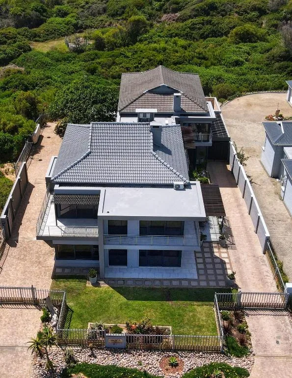 Modern two-story house with gray tile roof and brick driveway, surrounded by green landscape