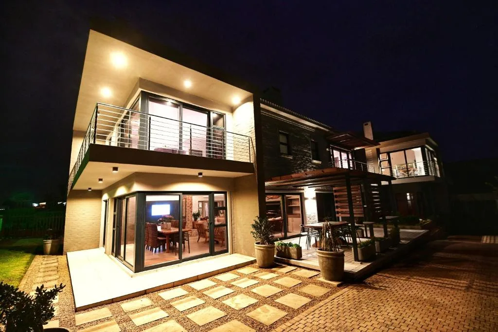 Modern holiday home exterior at night with illuminated deck and garden pathways