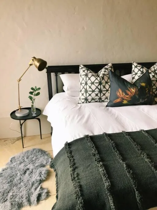 Modern bedroom with white linens, patterned pillows, and dark green throw blanket