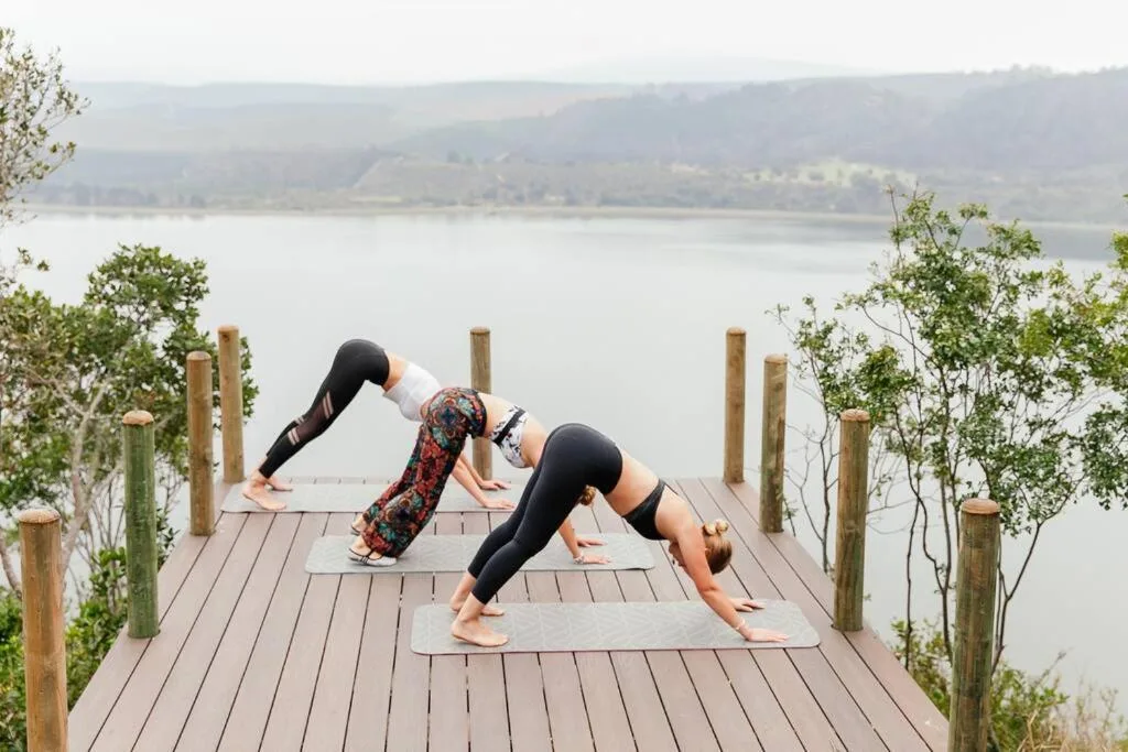 Two women doing yoga on wooden deck overlooking lagoon with mountains