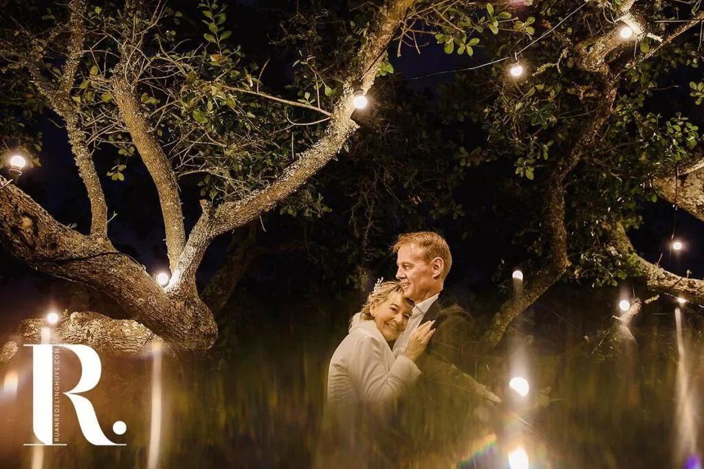 Couple embracing under illuminated trees at night on property grounds