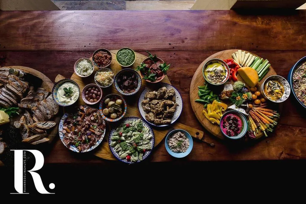 Overhead view of gourmet spread with grilled fish, vegetables, dips, and charcuterie on wooden table