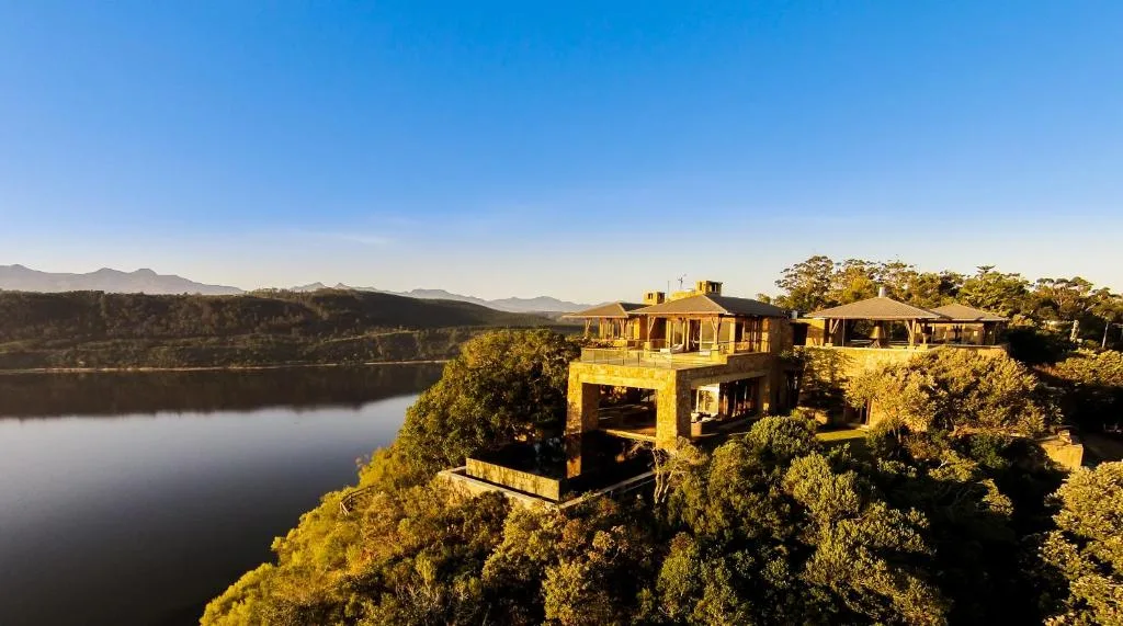 Luxury villa perched on forested cliff overlooking calm lagoon and distant mountains