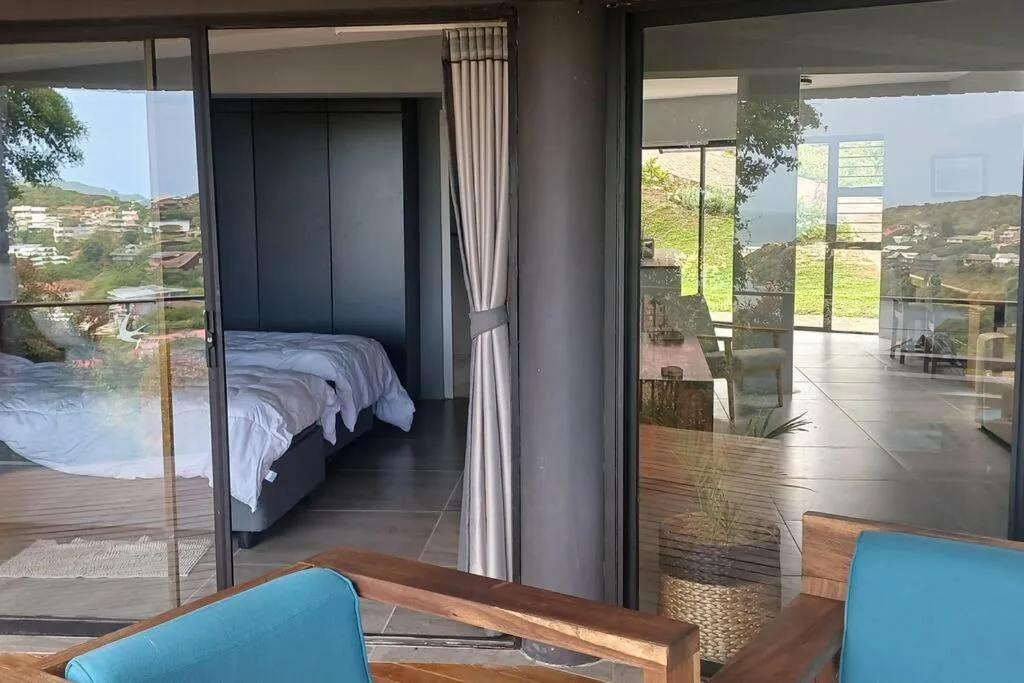Modern bedroom with bed visible through glass doors and hillside views beyond
