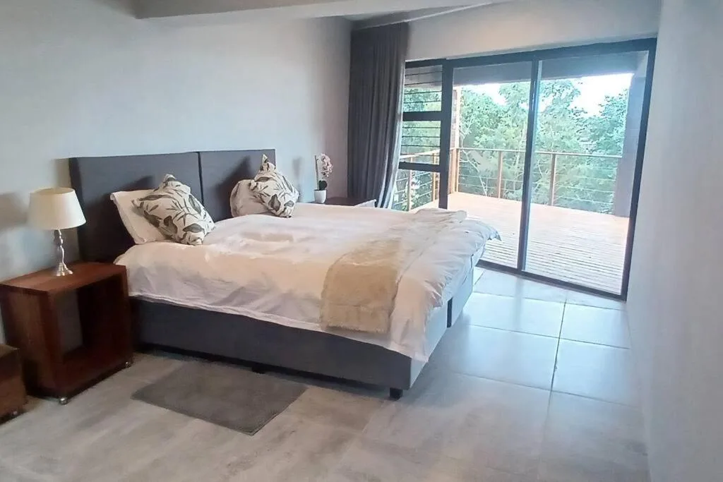 Modern bedroom with queen bed, forest views through sliding glass doors