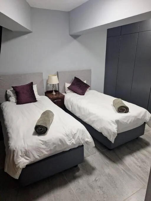 Twin bedroom with white linens, purple pillows, and dark wardrobe.