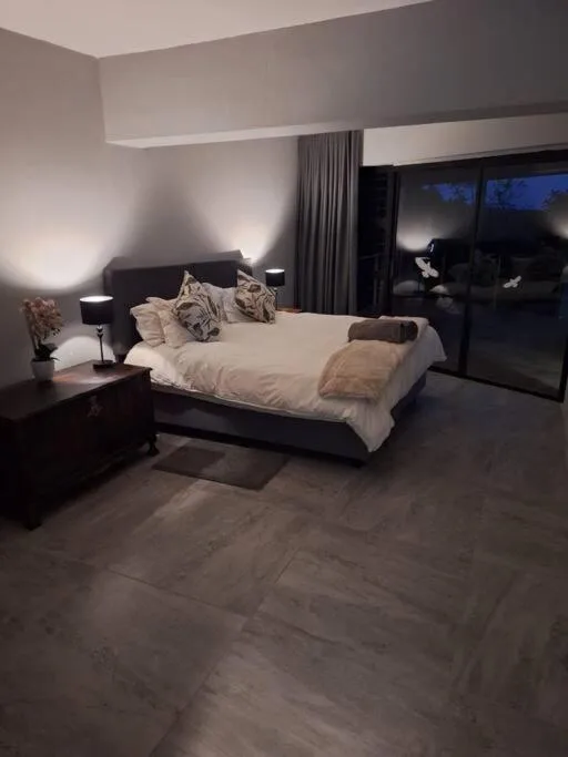 Modern bedroom with queen bed, ambient lighting, and large windows overlooking dusk