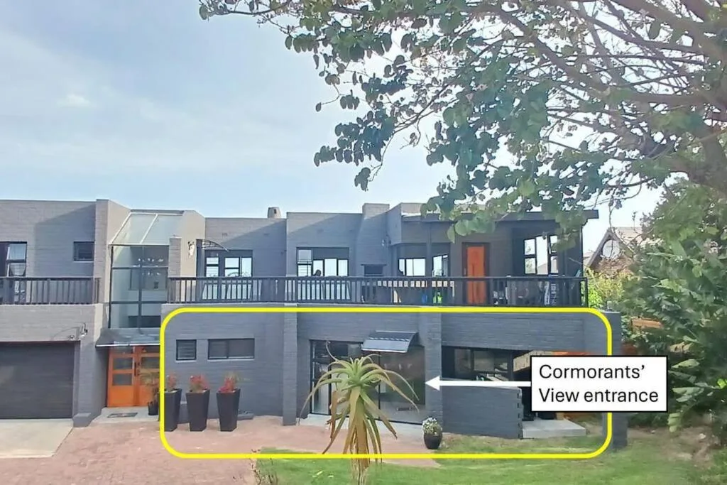 Modern gray self-catering home facade with orange accents and landscaped entrance