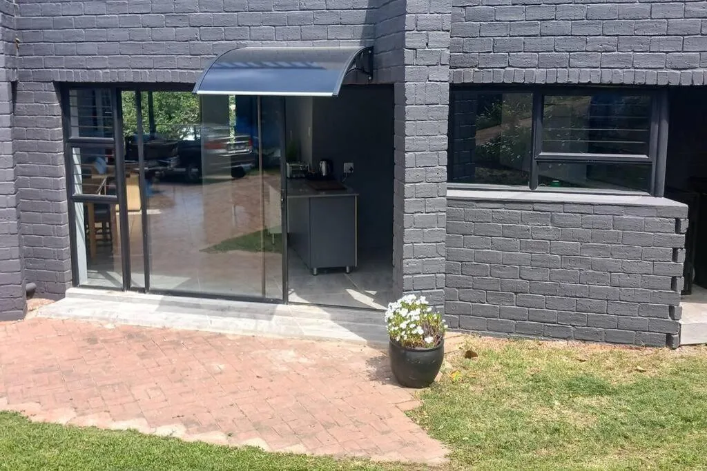 Modern dark brick facade with glass sliding doors and manicured lawn entrance