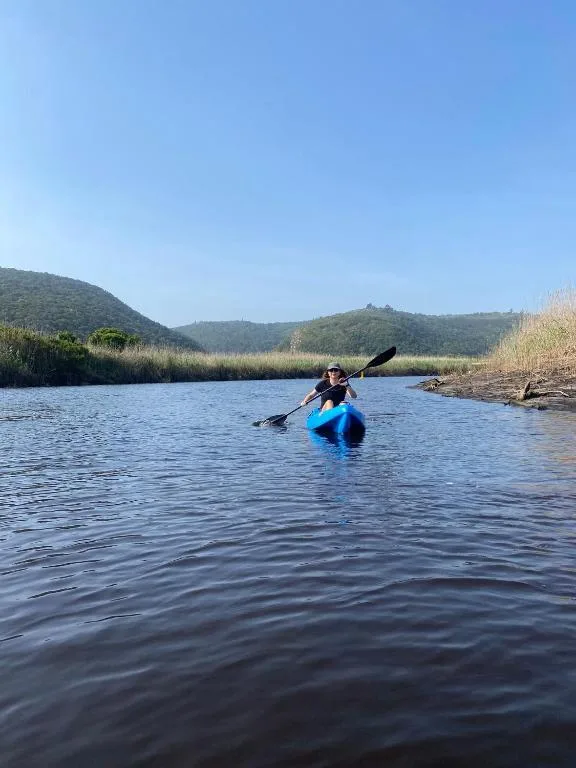 Kayaker paddling on lagoon surrounded by green hills and reeds