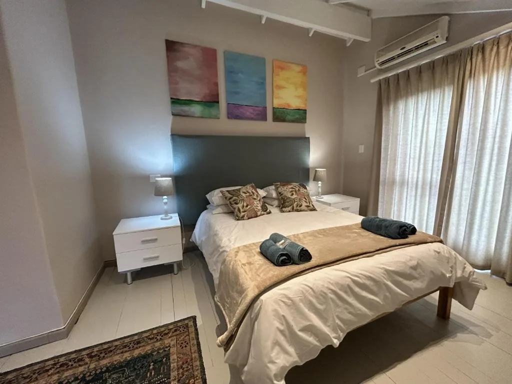 Spacious bedroom with queen bed, dark headboard, colorful artwork, and air conditioning unit