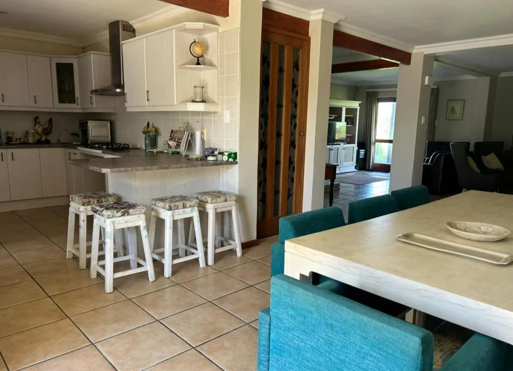 Open-plan dining and kitchen area with teal upholstered chairs and white cabinetry