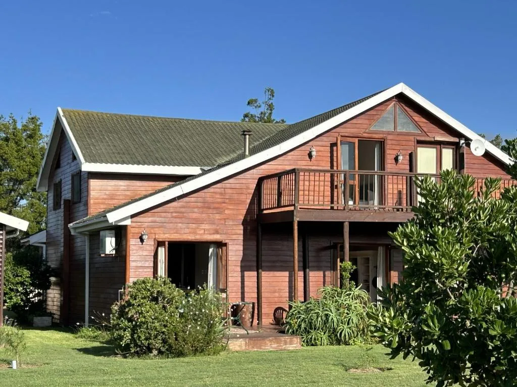 Red wooden cottage with white trim, upper deck, green lawn and landscaping