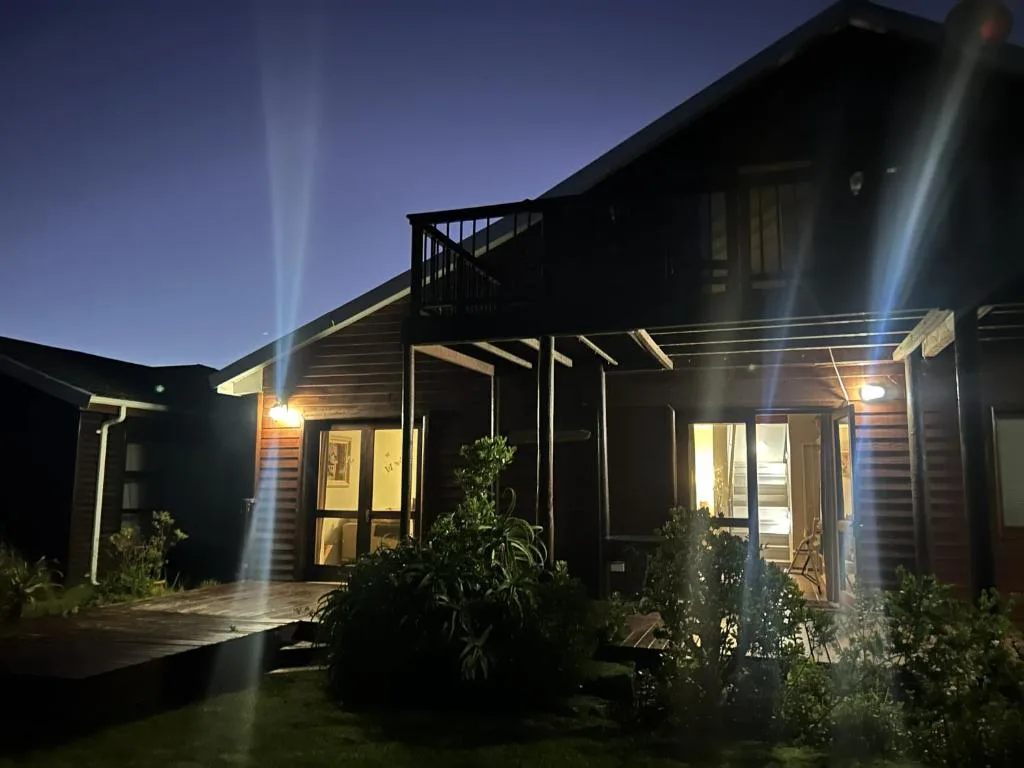 Modern cottage exterior illuminated at dusk with wooden deck and landscaping