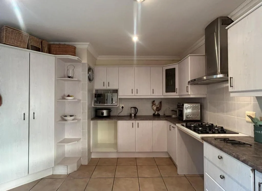 Modern white kitchen with gas range, stainless steel hood, and dark countertops