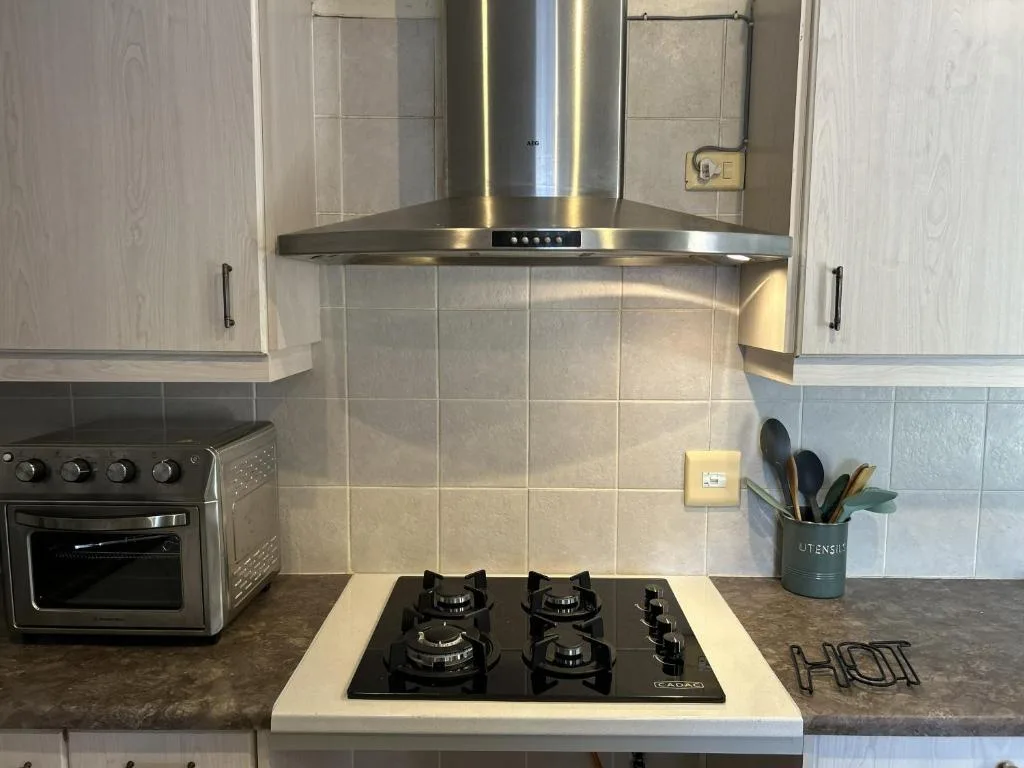 Modern kitchen with gas cooktop, stainless steel range hood, and tiled backsplash