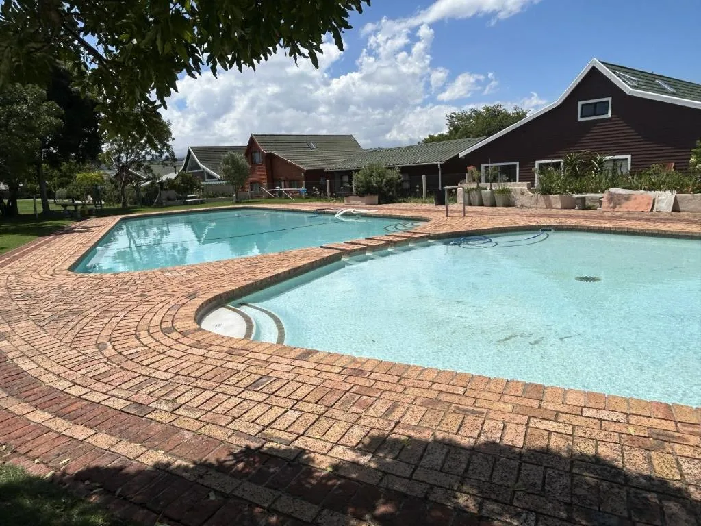 Two sparkling swimming pools with brick paving and dark-roofed buildings beyond