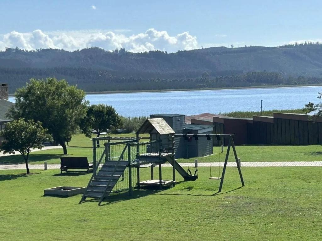 Lakeside view with forested mountains, green lawn, and play equipment