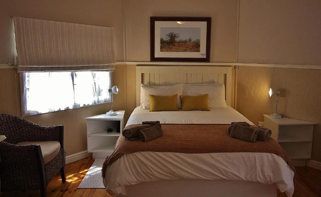 Warm bedroom with queen bed, wooden paneling, and framed landscape artwork