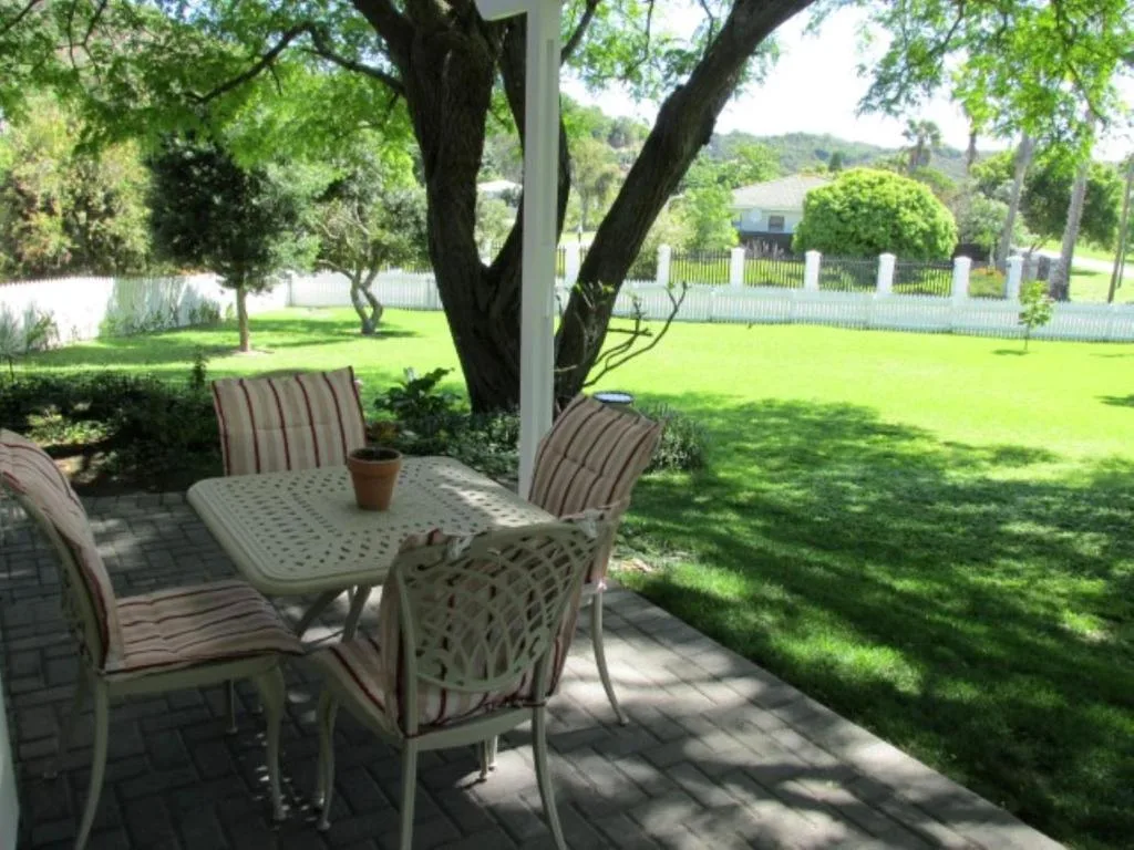Shaded patio with dining table and chairs overlooking manicured lawn