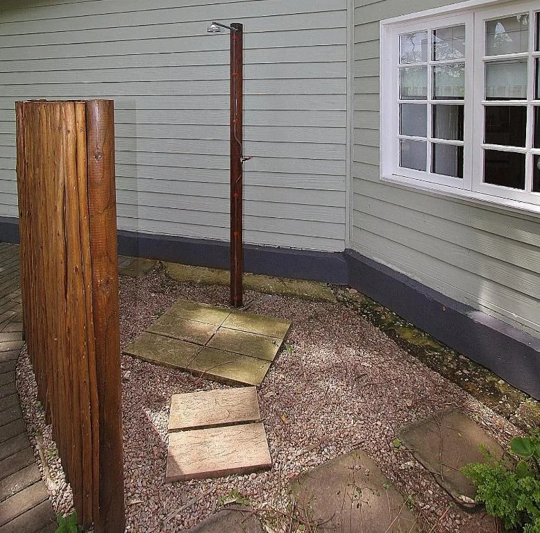 Outdoor shower area with wooden posts and gravel pathway beside cottage
